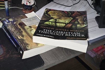 Two well-used theology books on a desk, resting on a stack of printed notes