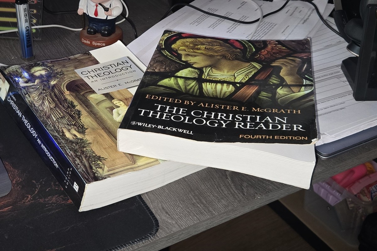 Two well-used theology books on a desk, resting on a stack of printed notes
