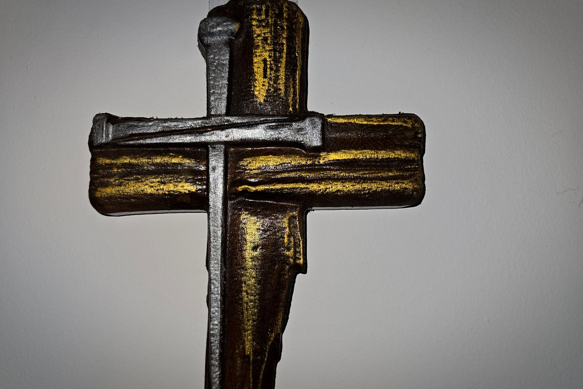 A wooden cross with an iron nail laid across it, hanging on a wall